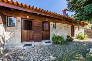 Un edificio rústico de piedra con tejado de tejas, dos puertas de madera y un patio empedrado.