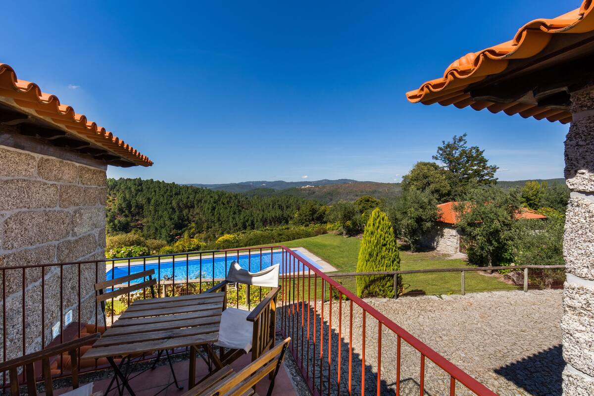 A balcony with a view of a swimming pool, stone walls, and a red railing.