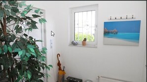 Ett rum med en krukväxt, ett fönster med utsikt över havet, en målning av en strand och ett element.