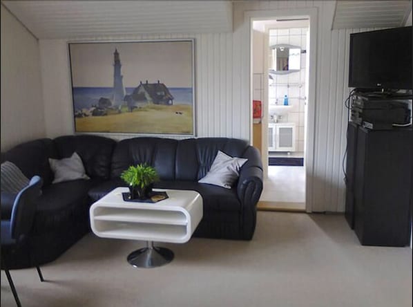 A living room with a black leather sofa, a white coffee table, and a painting of a lighthouse.