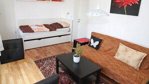 Ett kompakt bostadsutrymme med en säng, en soffa, ett matbord och ett litet soffbord.
