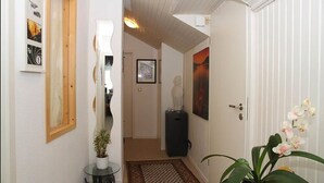 En hall med en trädörr, en inramad tavla, en krukväxt och en matta.