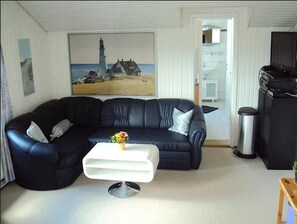 A living room with a black leather sofa, a white coffee table, and a painting of a lighthouse. - Apartments Reutlinger Strasse (Stuhr)