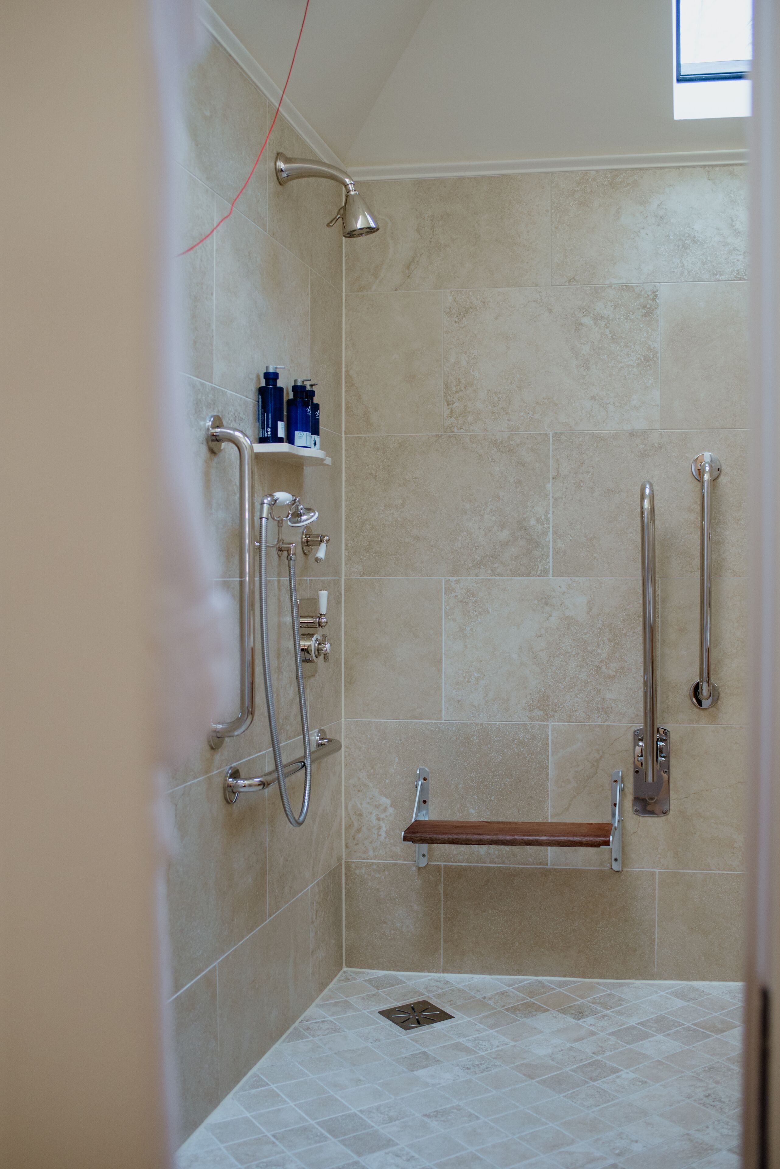 A shower with grab bars, a shelf with toiletries, and a window.