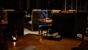 Un restaurante tenuemente iluminado con muebles de madera y una vela sobre la mesa.