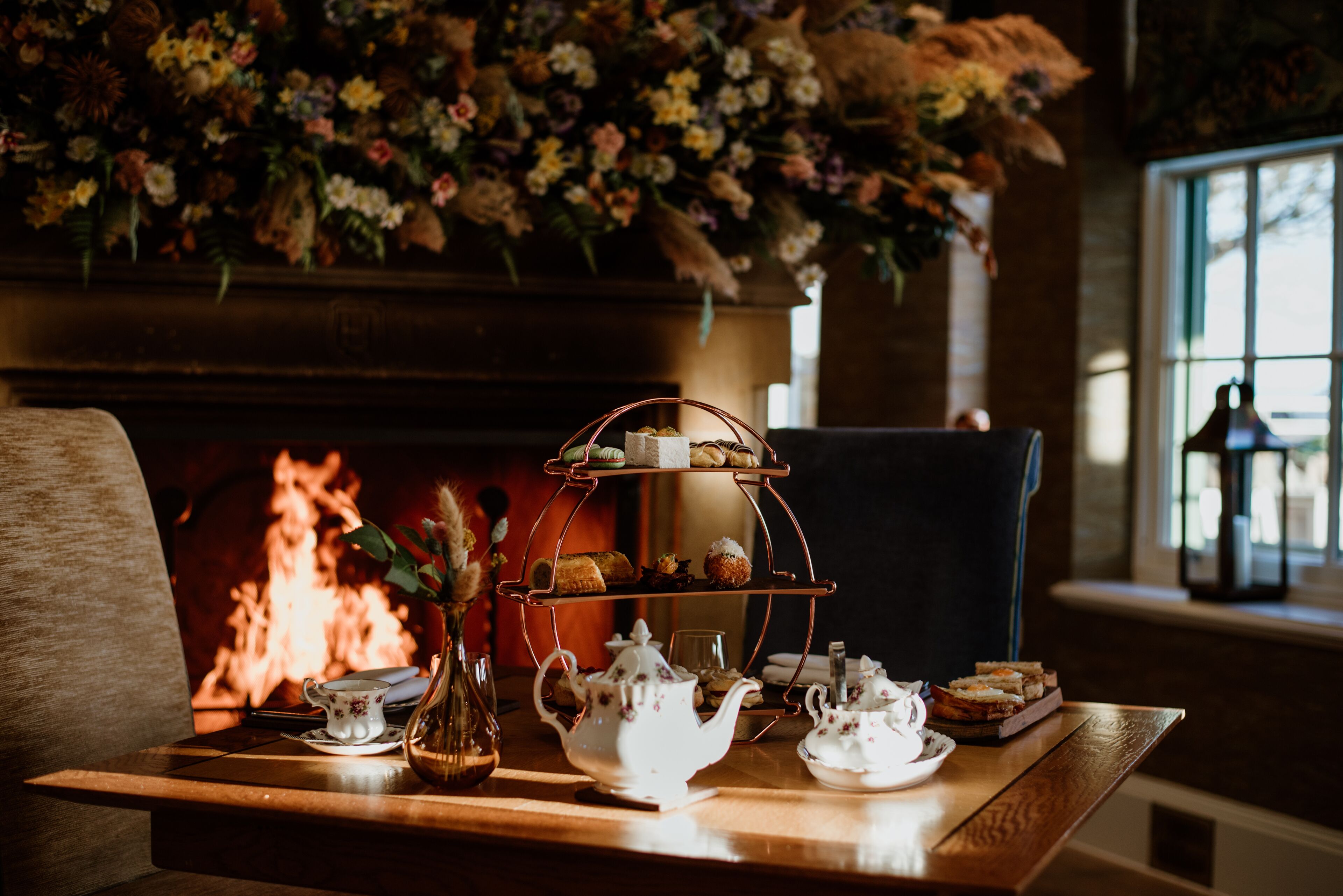 Uma mesa com um bule, xícaras, uma bandeja de doces e um vaso de flores.