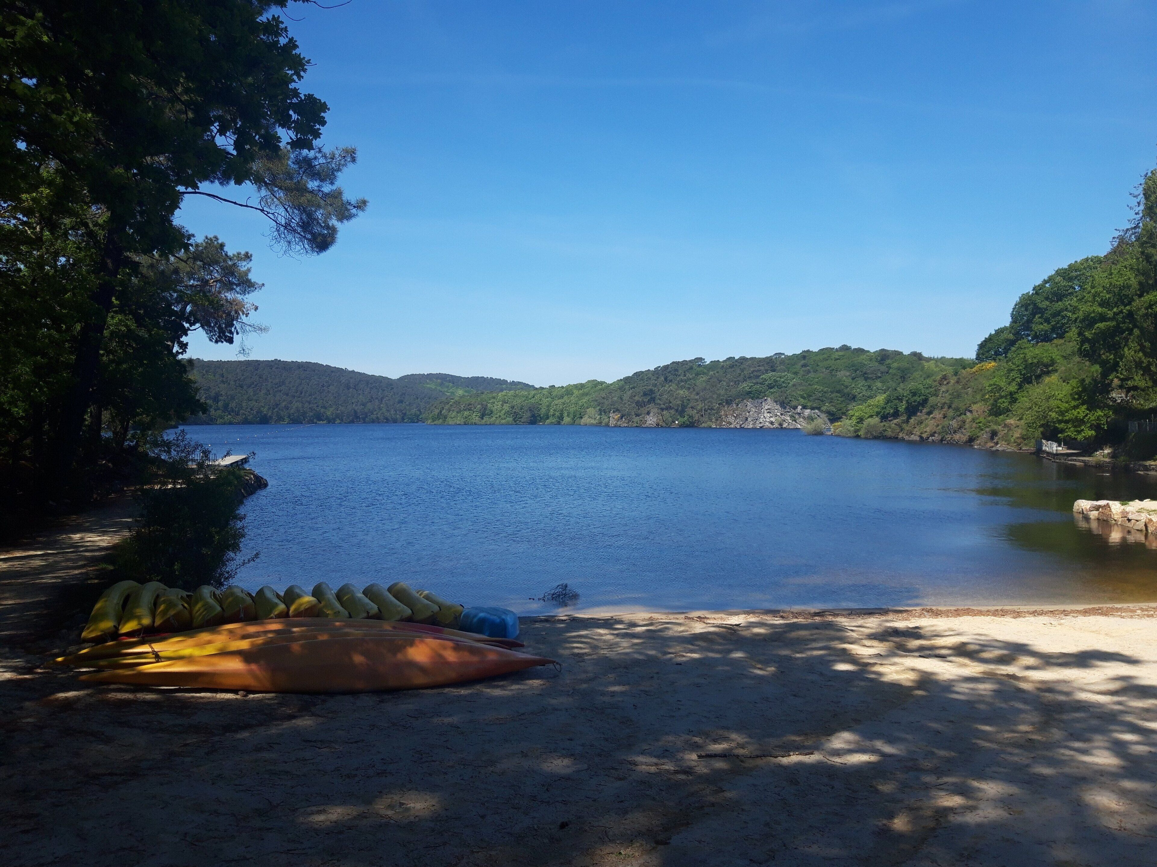 A calm lake surrounded by forested hills, a sandy beach, and a canoe.