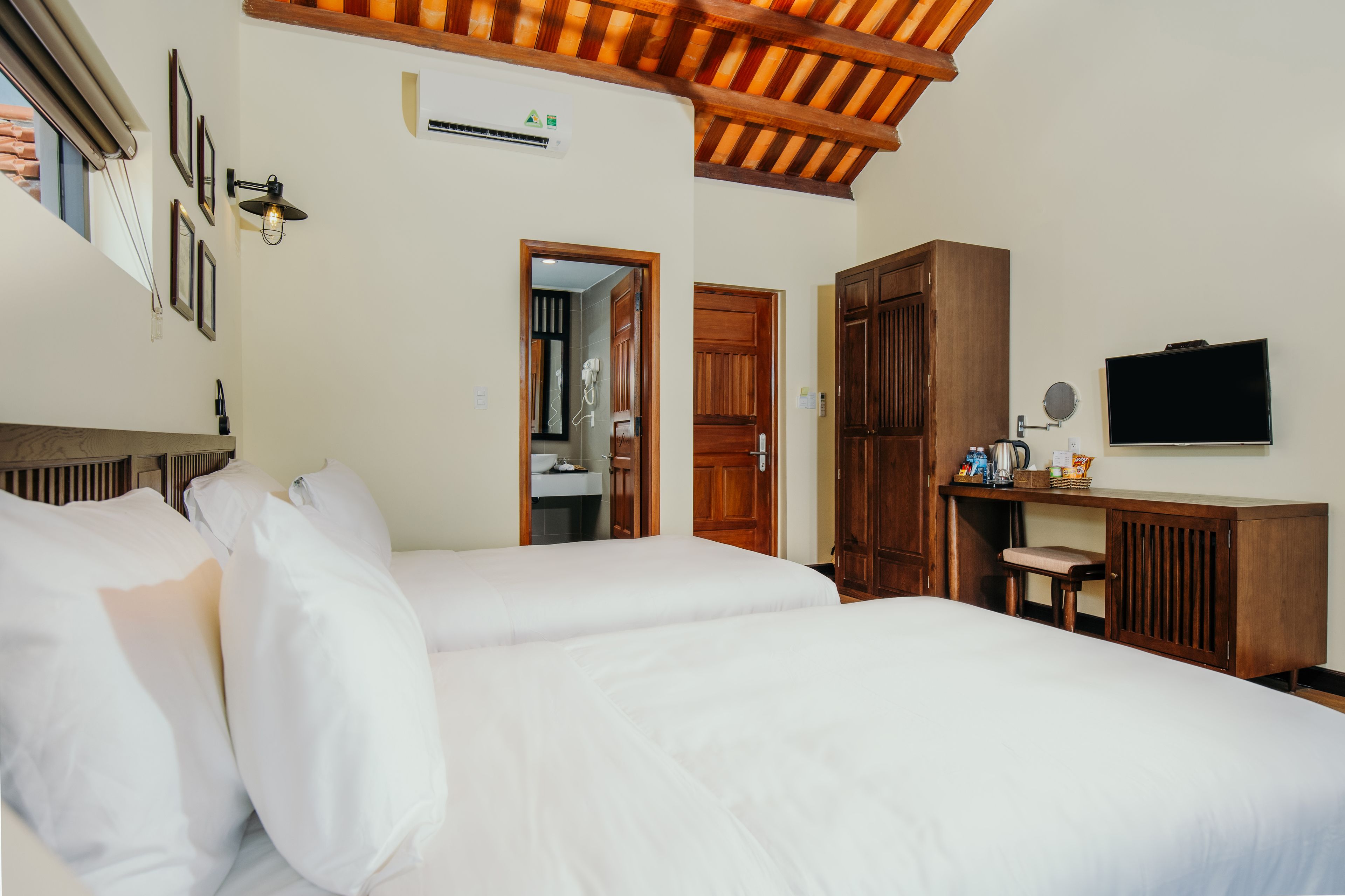 A hotel room with two beds, wooden furniture, a desk, a television, and a bathroom visible through an open door.