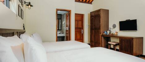 A hotel room with two beds, wooden furniture, a desk, a television, and a bathroom visible through an open door.