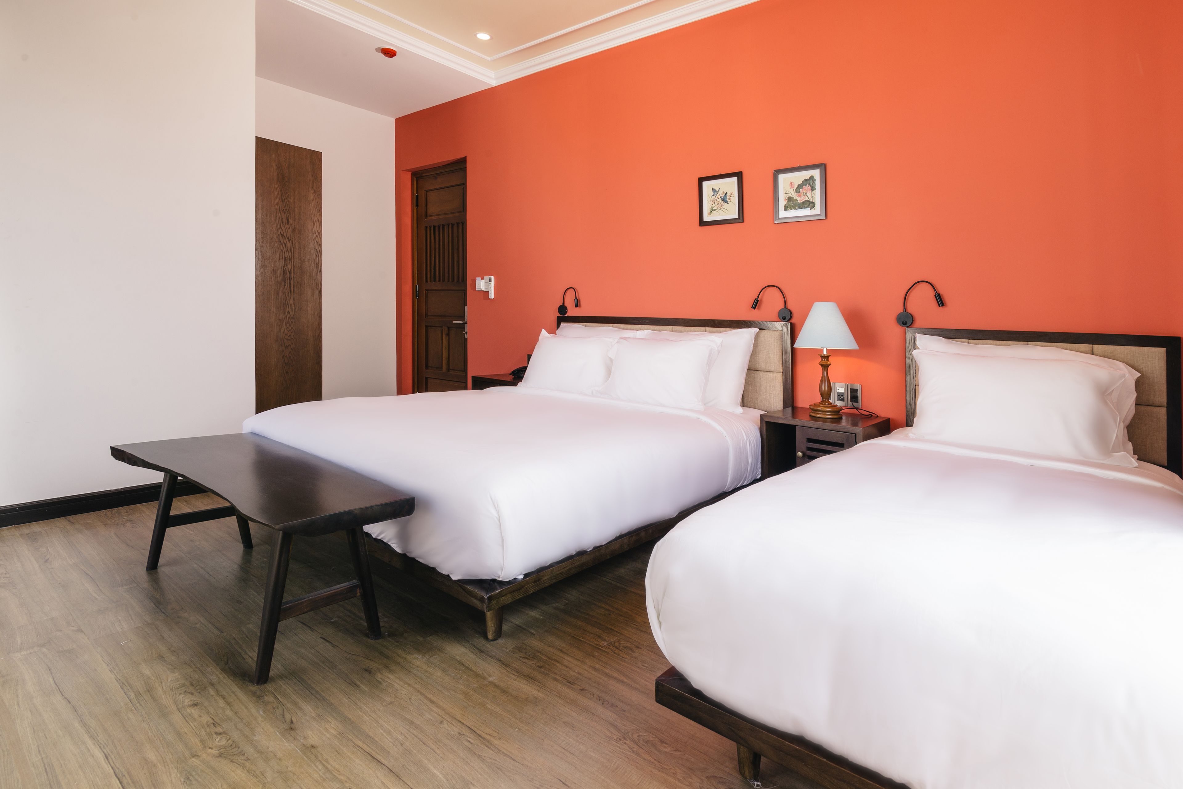 A hotel room with two beds, a wooden floor, and a red accent wall.