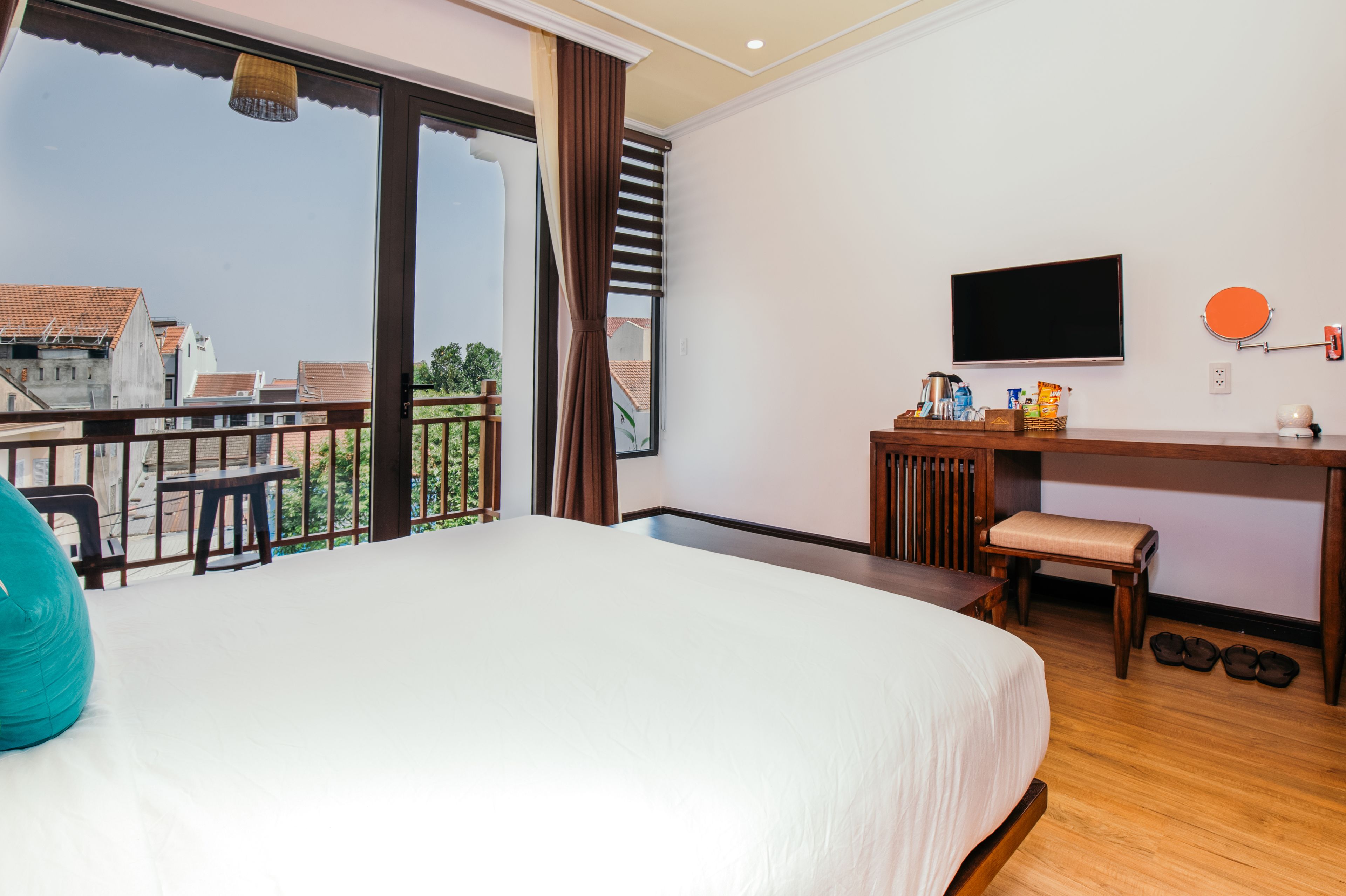Habitación de hotel con una cama grande, un escritorio con televisor y un balcón con vistas a edificios.