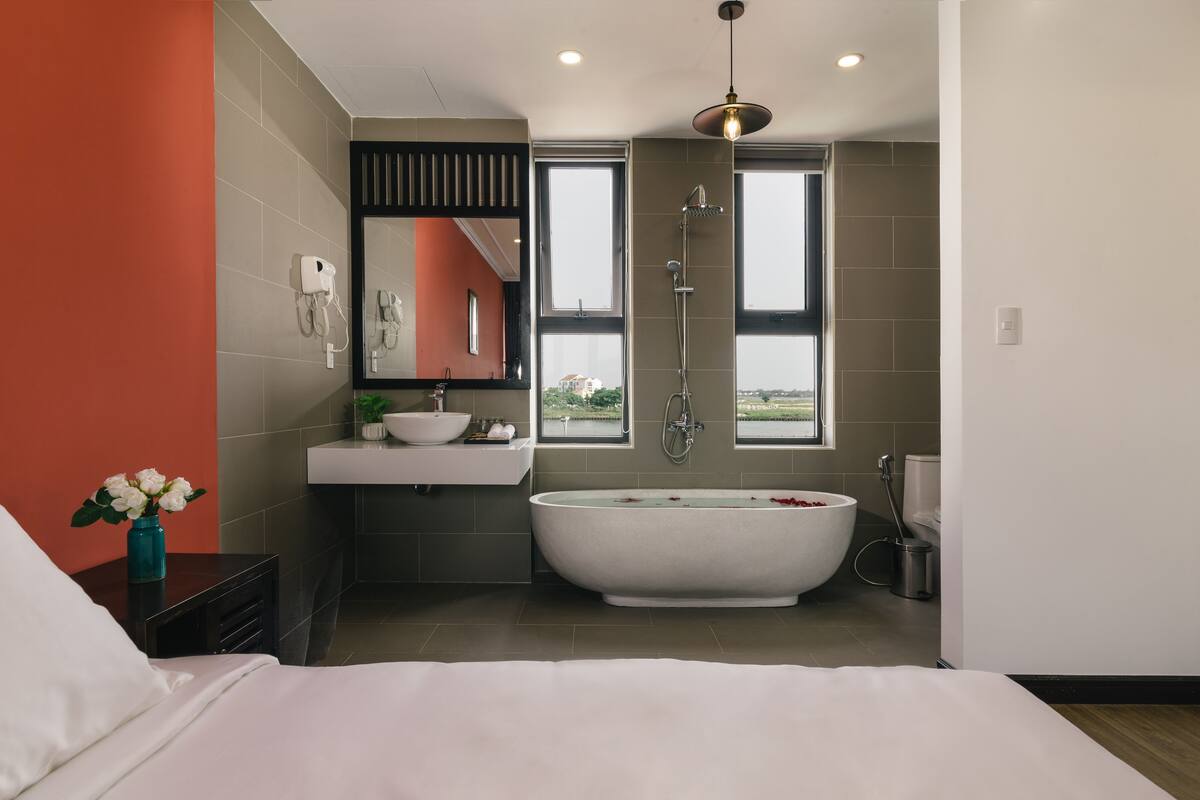 A modern bathroom with a freestanding bathtub, a large mirror, and a window providing a view of the city.