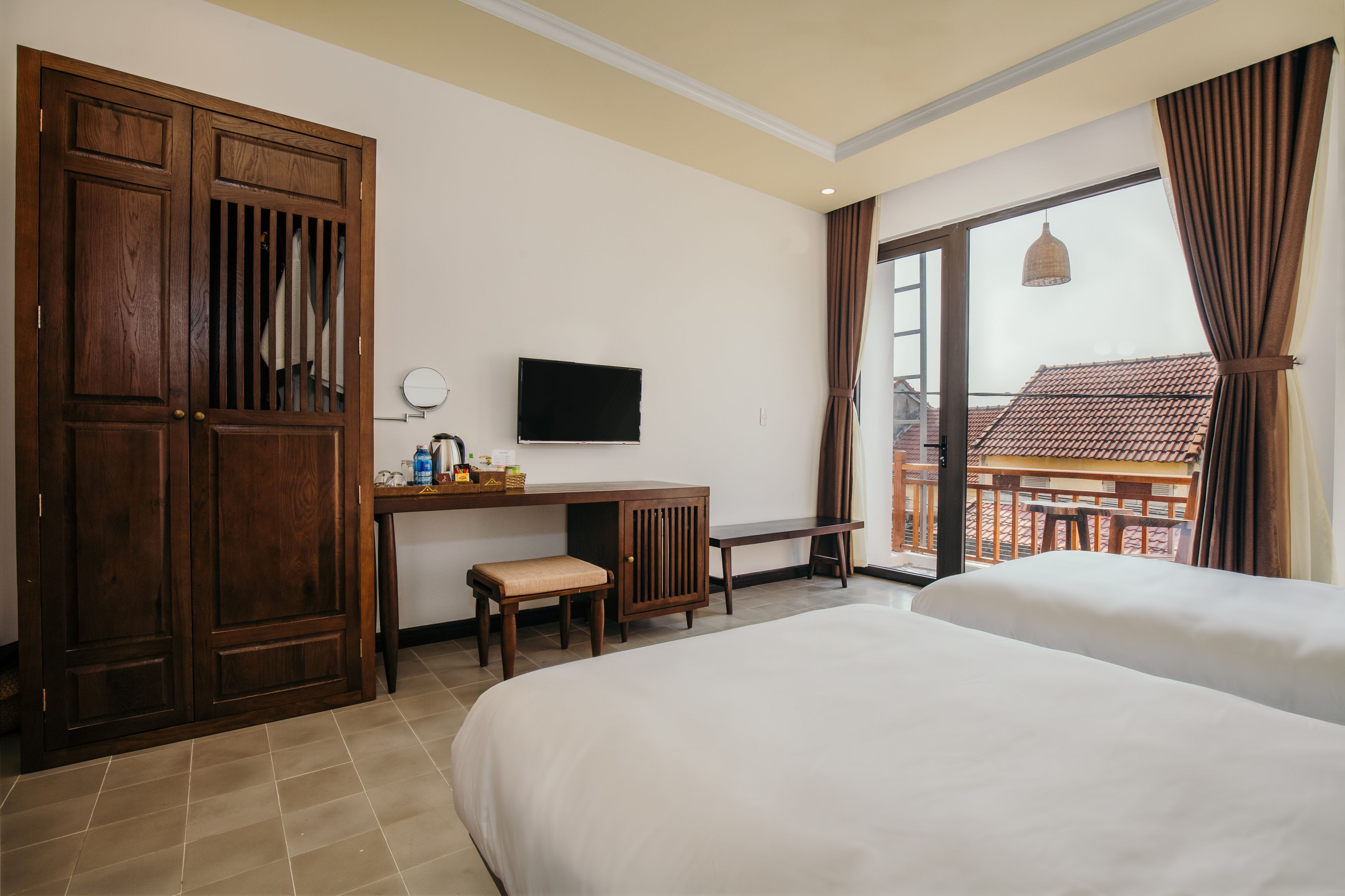 Ein Hotelzimmer mit zwei Betten, einem Schreibtisch mit Stuhl, einem Fernseher und einem Balkon mit Blick auf ein Gebäude.