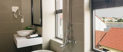 A modern bathroom with a freestanding bathtub, a shower, and a window with a view of buildings.