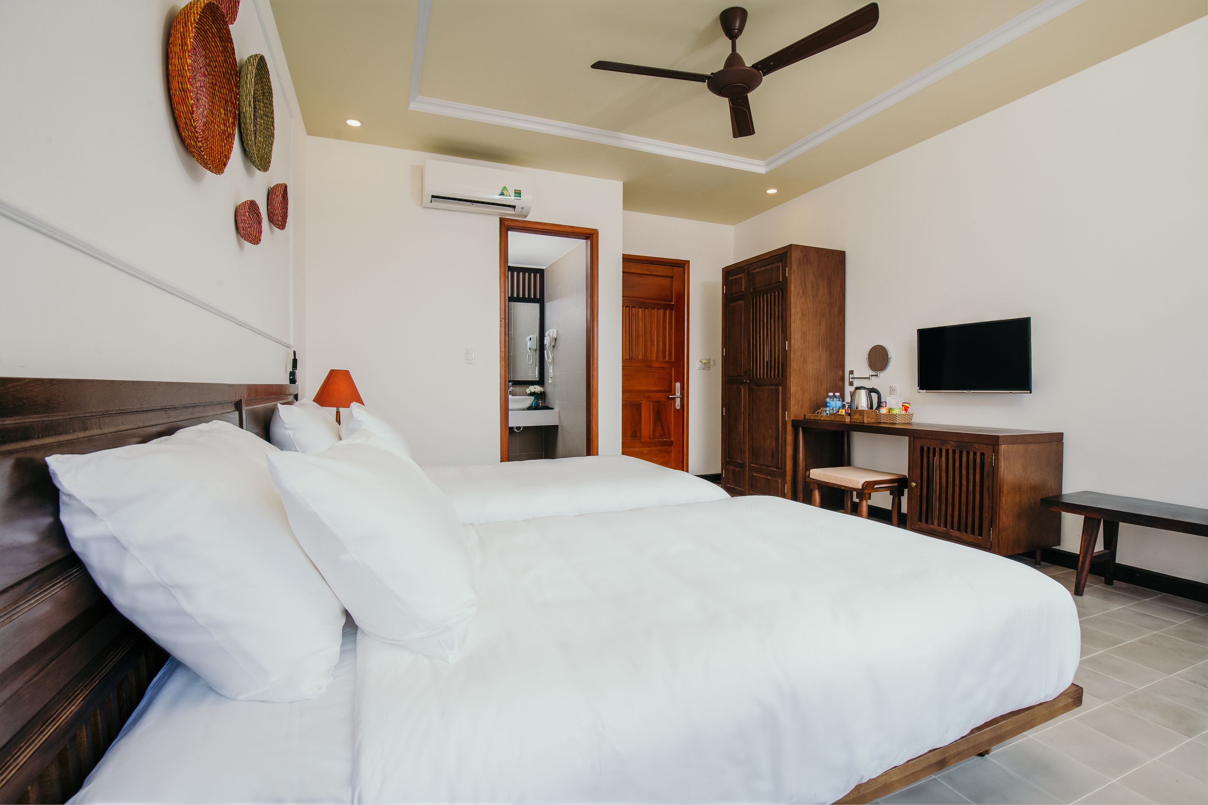 A hotel room with a large bed, a desk with a chair, a television, and a ceiling fan.