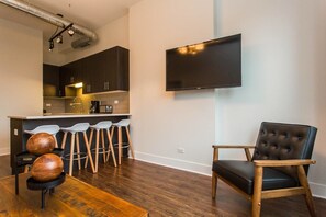 A modern living space with a kitchen area, a dining table with stools, and a single leather armchair. - Handsome Mccormick 3bd-2ba Loft (Chicago)