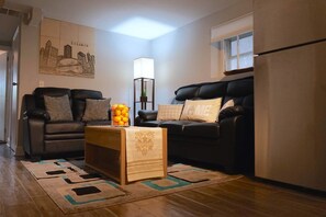 A living room with two black leather sofas, a wooden coffee table with a vase of oranges, a floor lamp, and a cityscape artwork on the wall. - The Karlov Connection - Ohare Wrigley Gateway (Chicago)