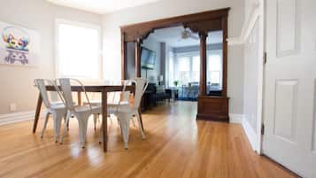 A spacious dining area with a wooden table and white chairs, leading to a kitchen and living area with a view of the outdoors.