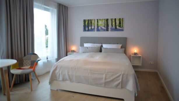 Une chambre à coucher moderne avec un grand lit, une chaise, une petite table et deux lampes de chevet.