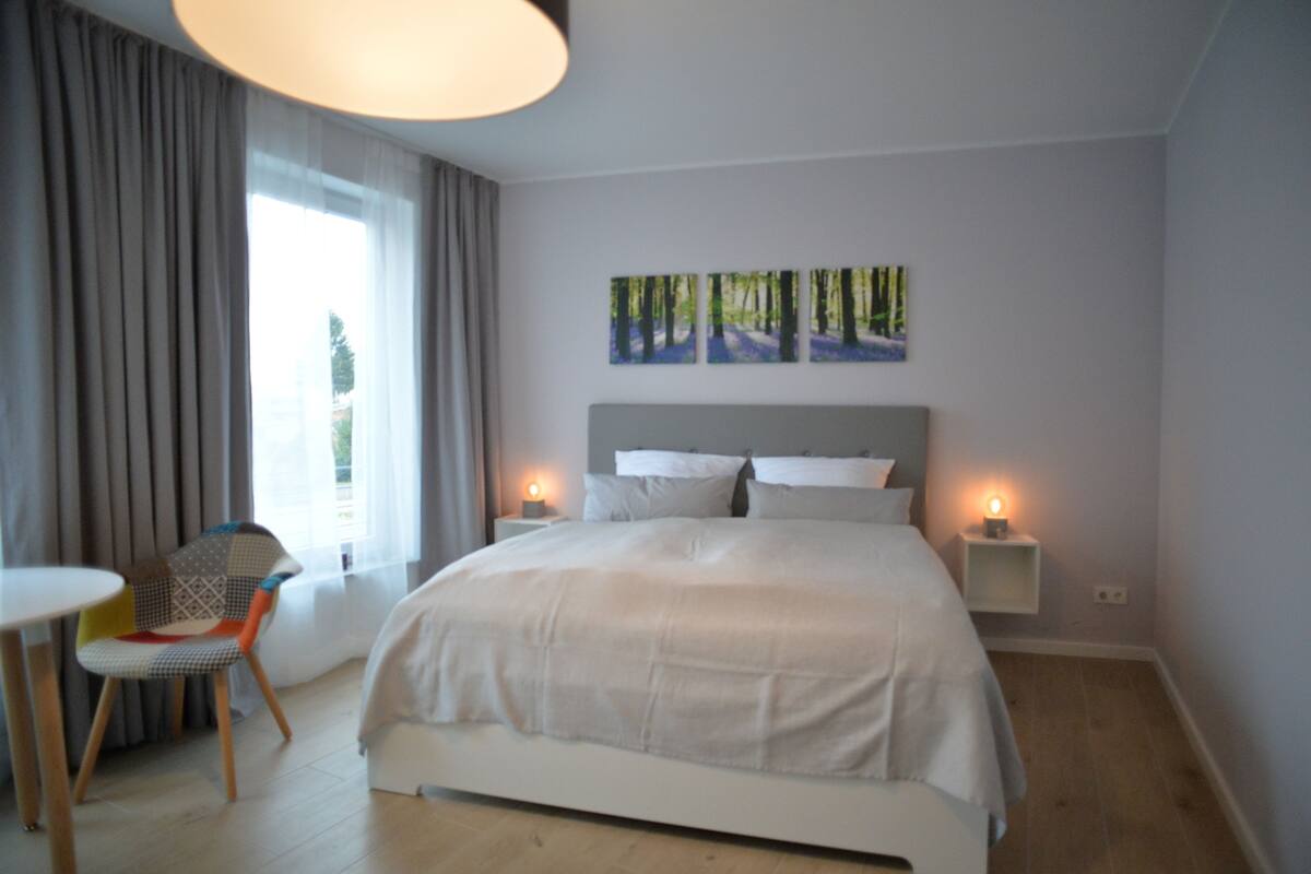 Quarto moderno com uma cama grande, uma cadeira, uma mesinha e duas luminárias de cabeceira.