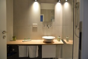 A modern bathroom with a large sink, mirror, and shower. - Grey House Apartments Grossbeeren (Grossbeeren)