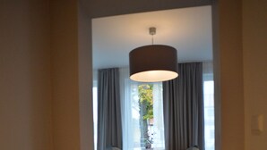 Une chambre d’hôtel avec un lit, une table, deux chaises et une grande fenêtre avec des rideaux.