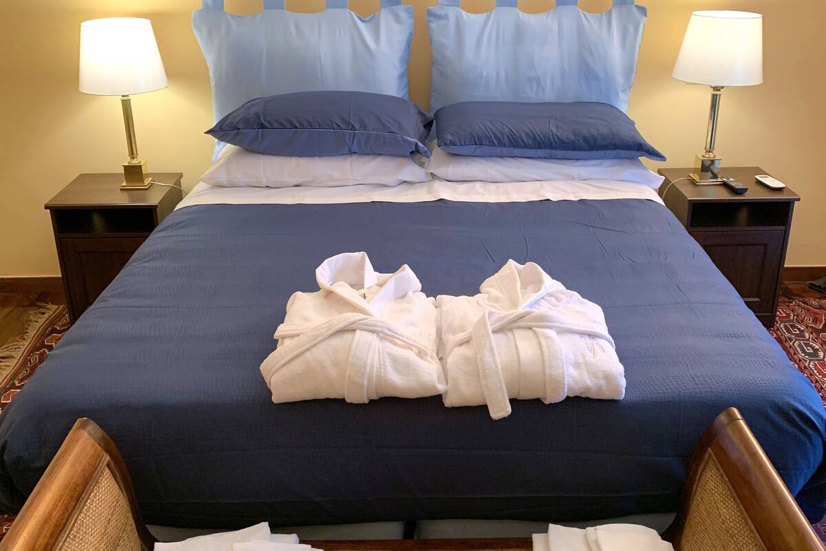 A hotel room with a large bed, two bedside tables with lamps, a framed artwork on the wall, and a patterned carpet.