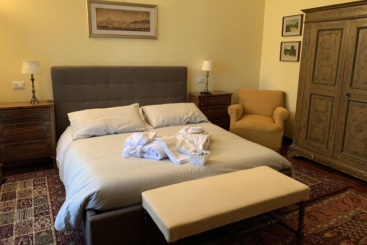 A hotel room with a large bed, a chair, a cabinet, and a rug.