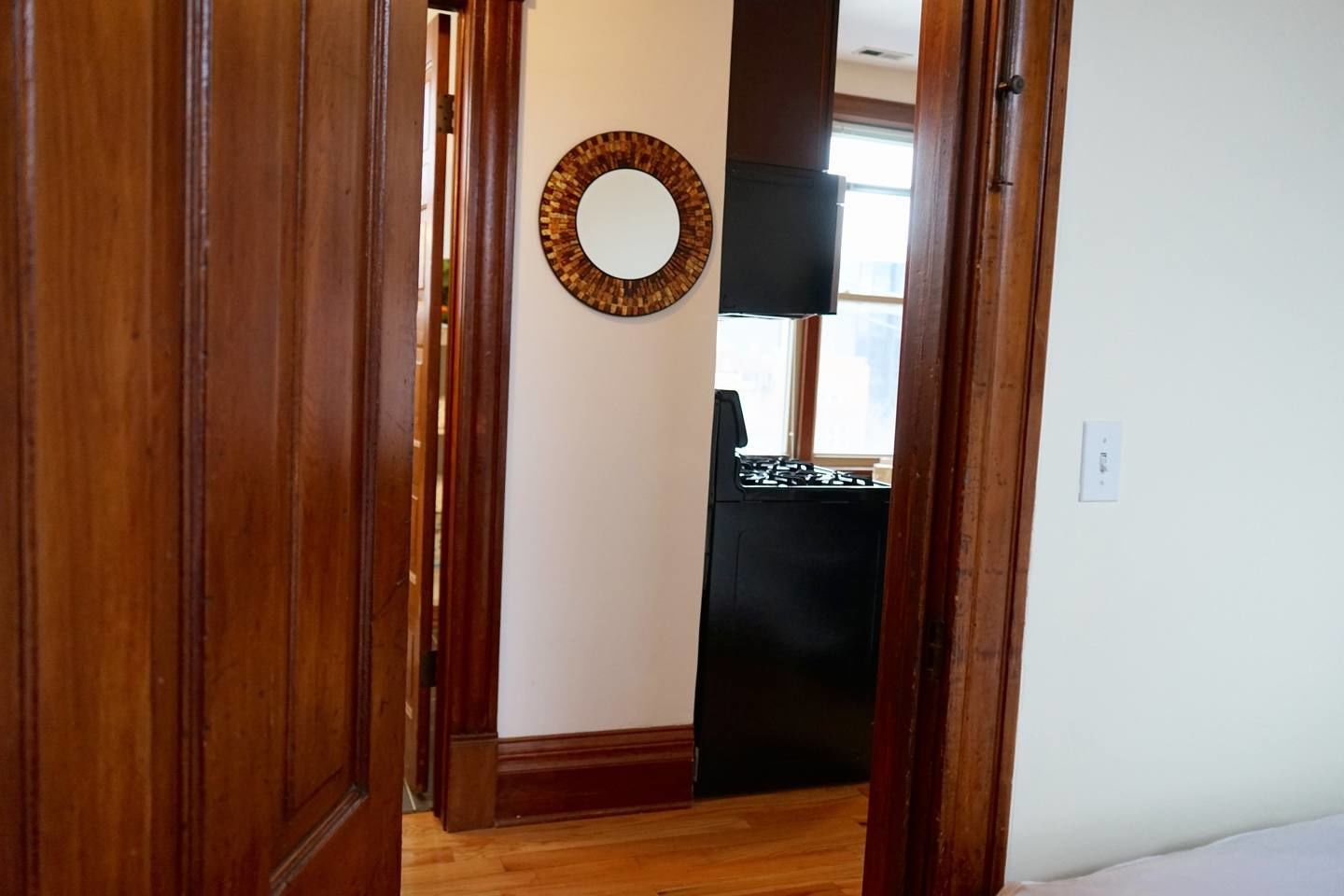 A hallway with wooden doors, a round mirror on the wall, and a black appliance in the background.
