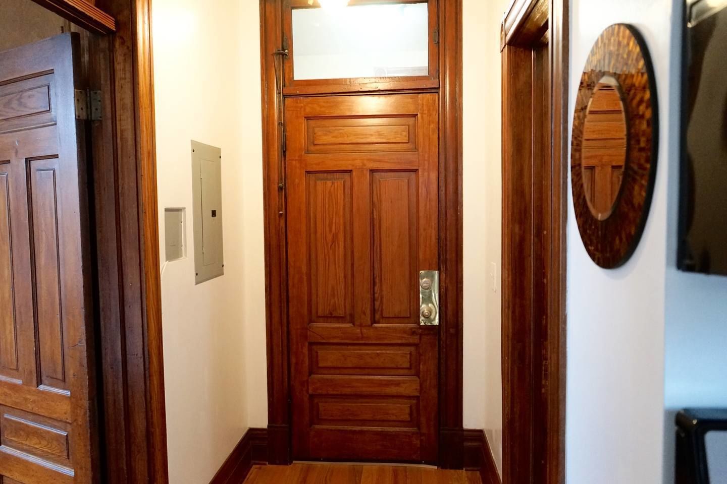 A wooden front door with a glass panel, a light switch, and a wall-mounted mirror.