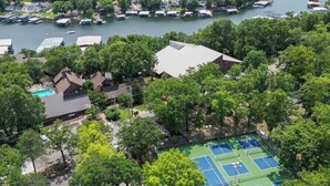 Vista aerea di un resort sul lago con numerosi pontili per barche, un campo da tennis e diversi edifici immersi in una fitta foresta.