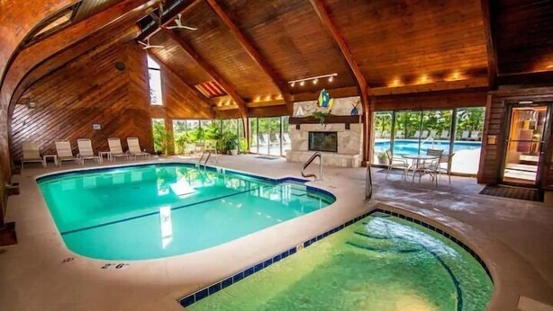 Una piscina interna con soffitto in legno e camino in pietra.