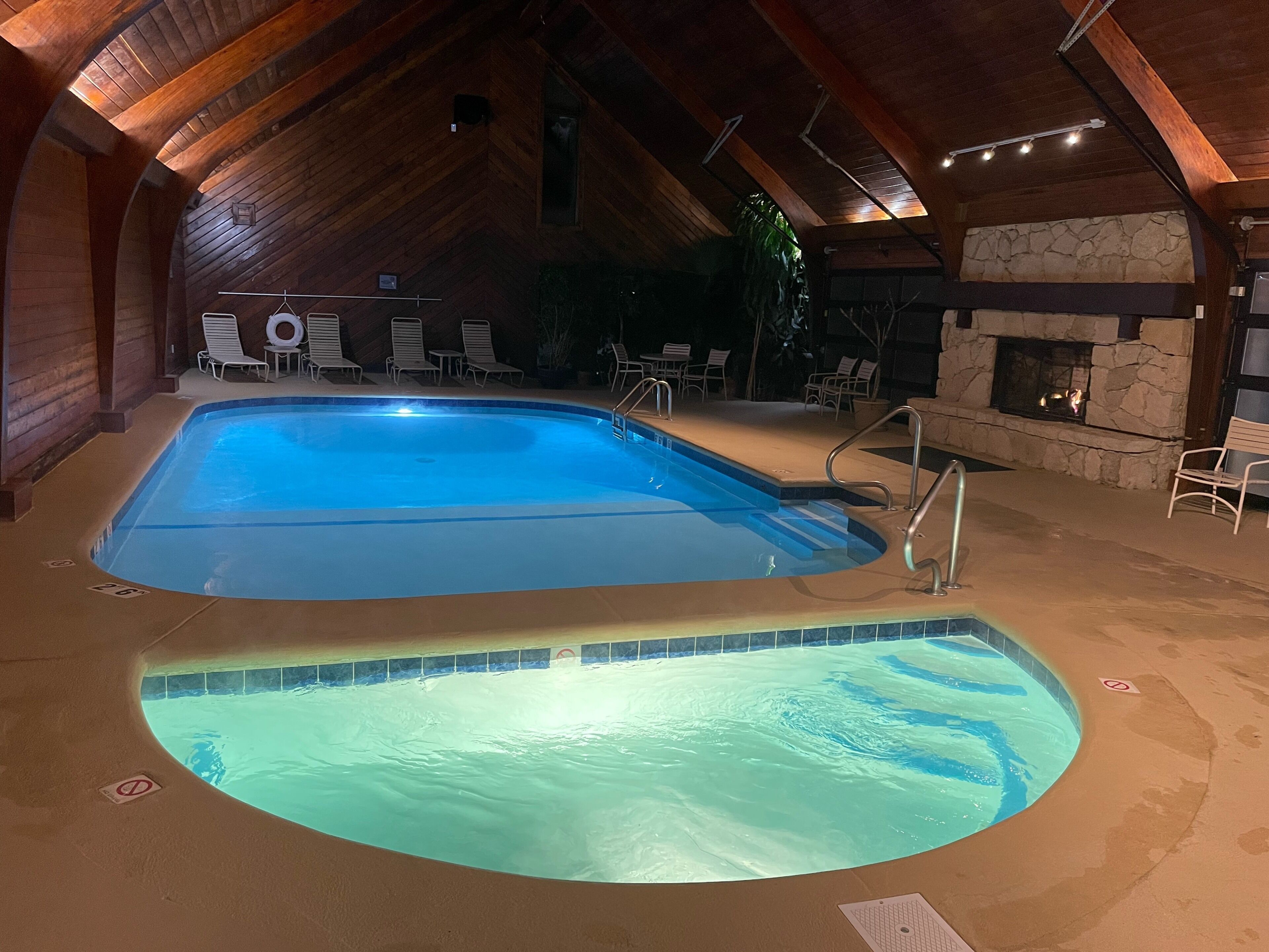 An indoor swimming pool with a stone fireplace and lounge chairs.