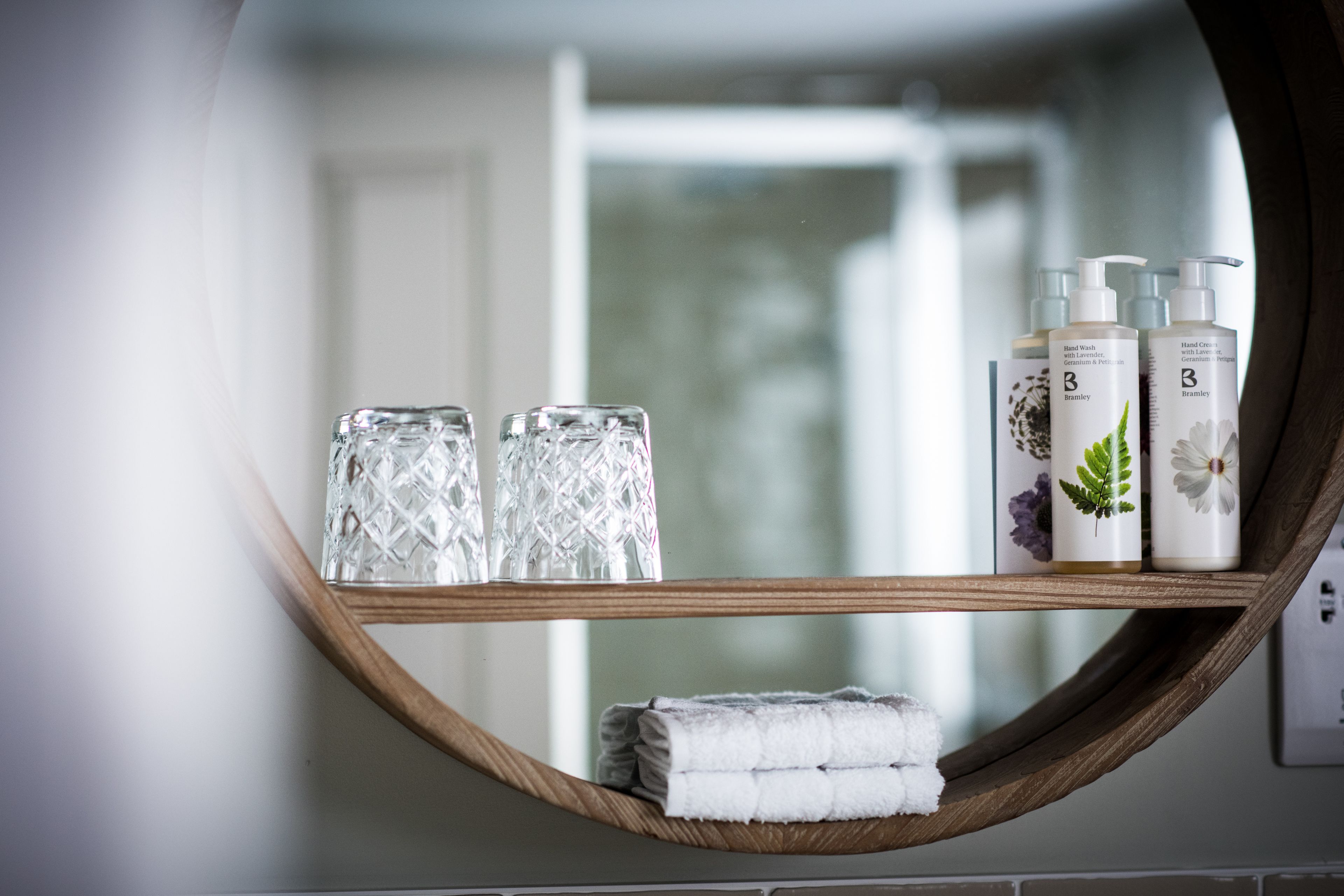 Une salle de bain avec une étagère en bois sur laquelle est posée une serviette pliée et trois flacons de savon liquide aux motifs de lavande et de rose.