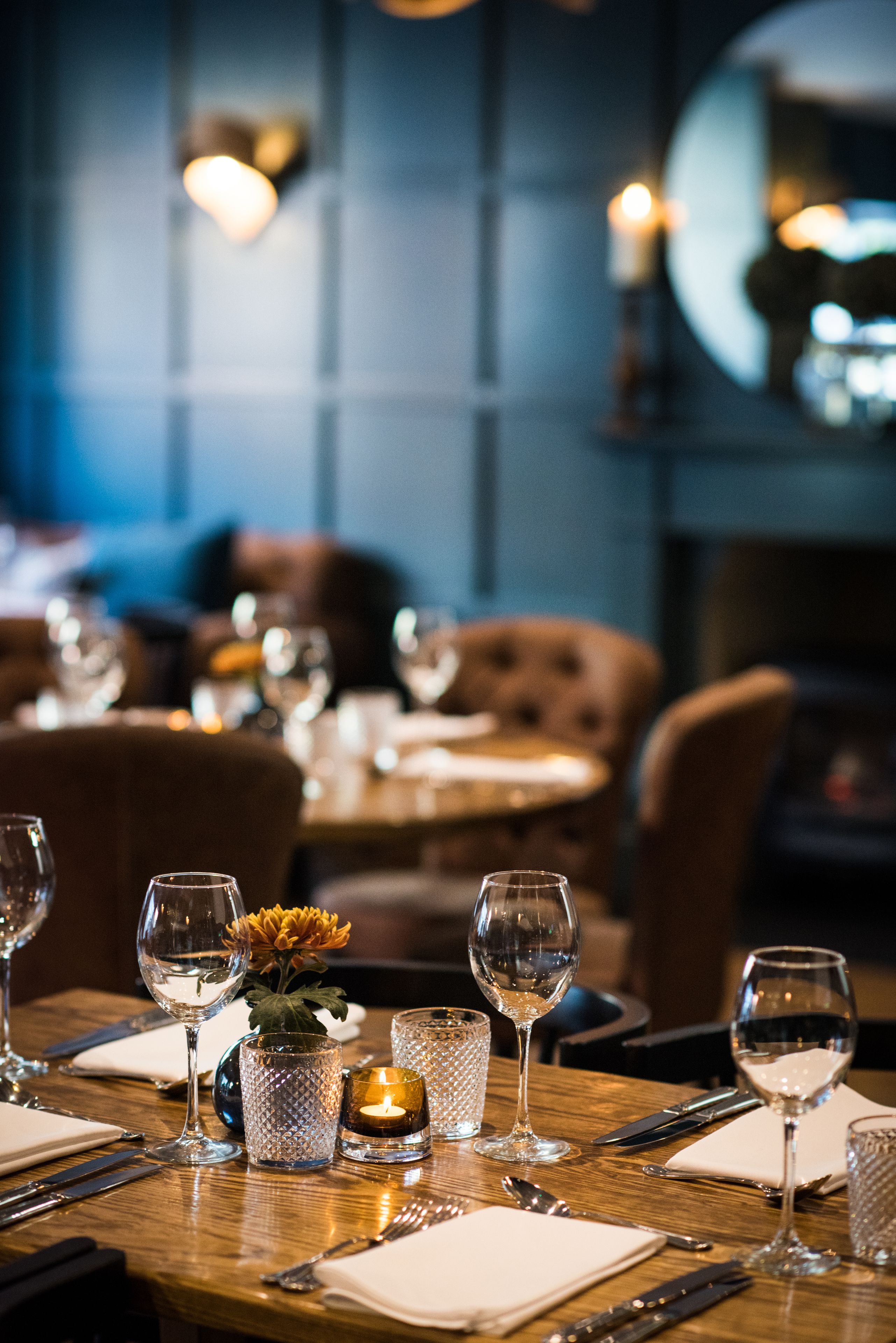 A restaurant setting with tables set for dining, featuring clear glassware, candles, and a vase with flowers.