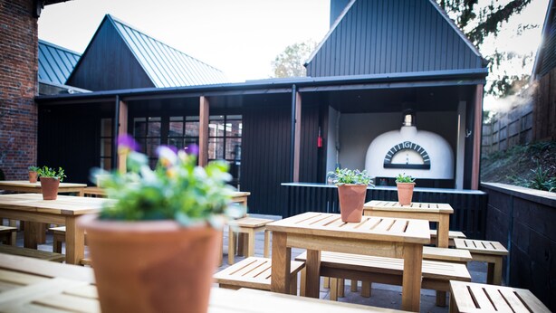 An outdoor seating area with wooden tables and terracotta planters. - The Fox (Winchester)