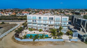 Un hotel de varios pisos con piscina en la azotea, rodeado de palmeras y vistas a la ciudad.