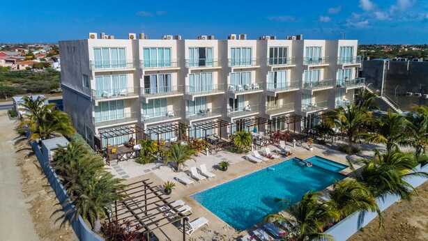 A multi-story hotel with a rooftop pool, outdoor seating, and palm trees. - Las Islas Aruba (Noord)