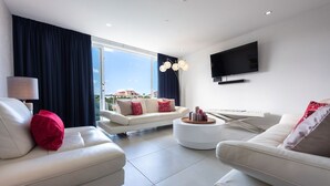 A modern living room with two white sofas, a round coffee table, and a flat-screen TV mounted on the wall. - Las Islas Aruba (Noord)