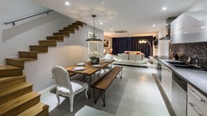 A modern kitchen with a built-in oven, a dining area with a wooden table and white chairs, and a staircase with wooden steps. - Las Islas Aruba (Noord)