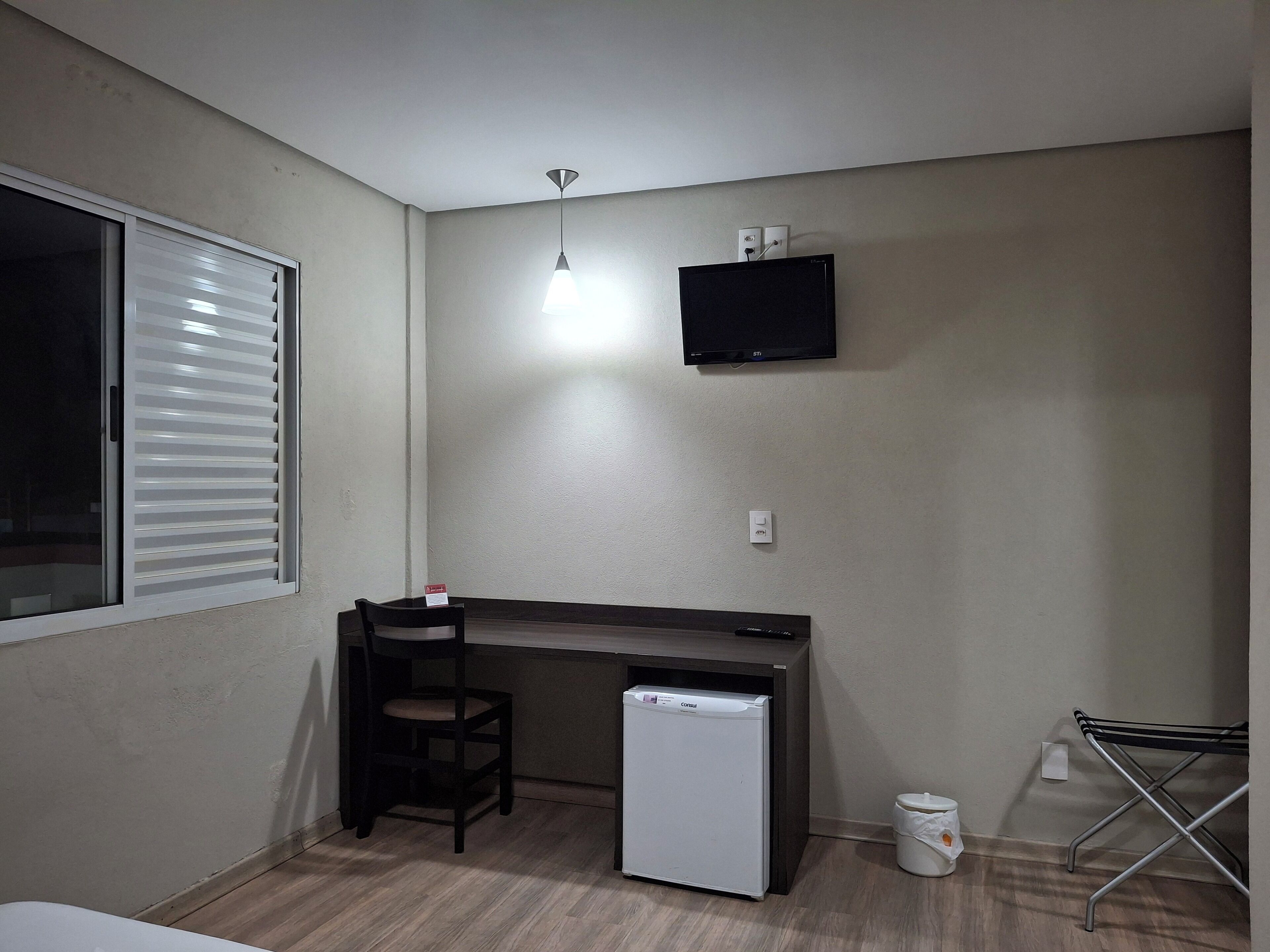 A small kitchenette with a refrigerator, a chair, a table, and a TV mounted on the wall.