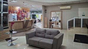 A modern reception area with a curved desk, a grey sofa, and a glass-top table. - Onix Inn Hotel Cravinhos (Cravinhos)