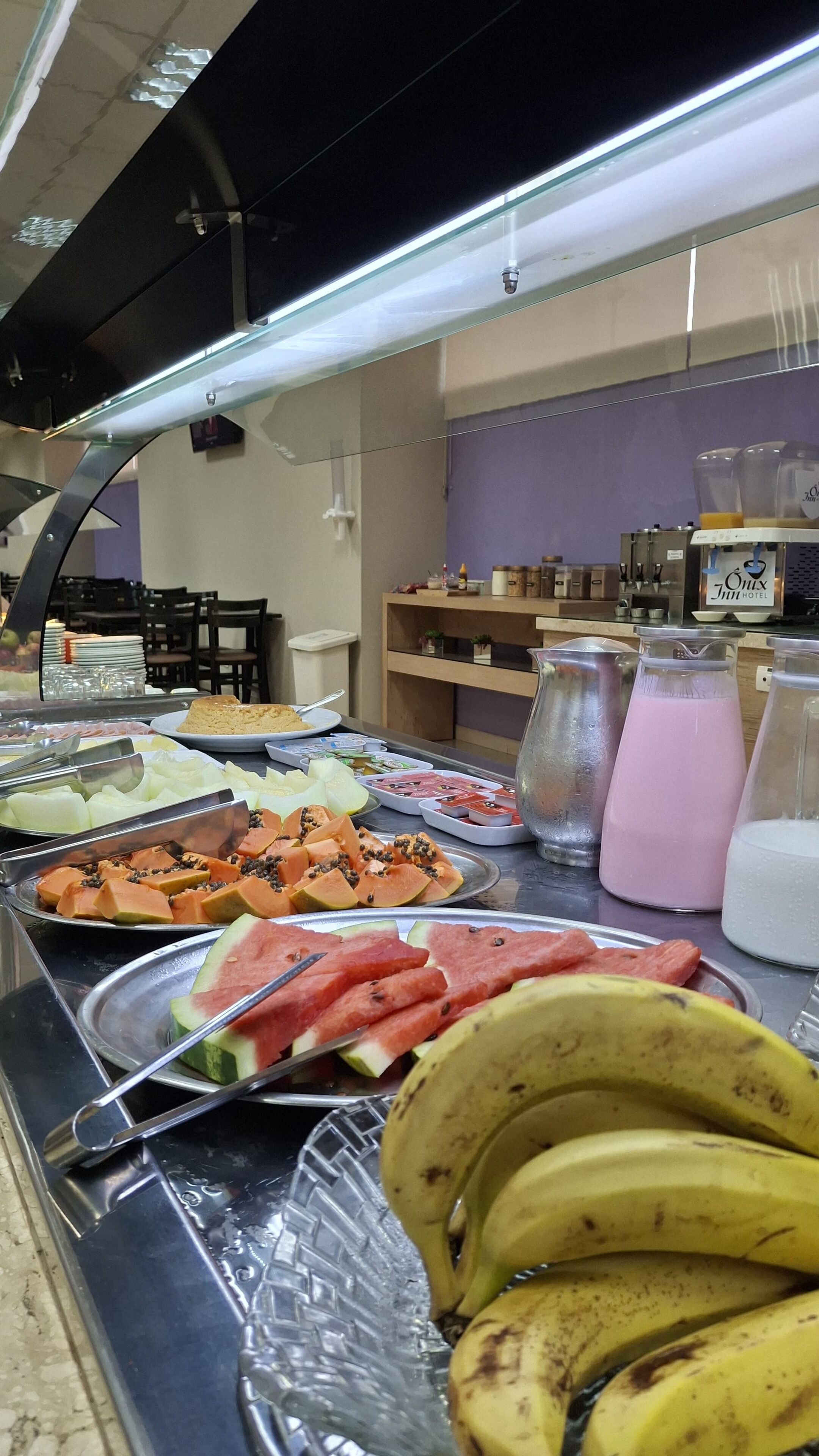 A buffet with various fruits and beverages, including watermelon slices, bananas, and a pink drink.
