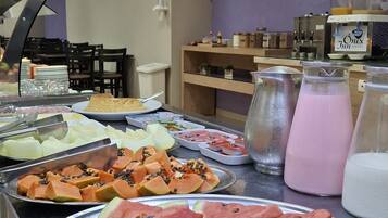 A buffet with various fruits and beverages, including watermelon slices, bananas, and a pink drink.