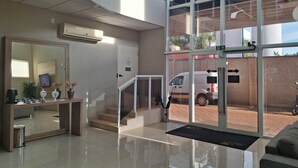 A modern hotel lobby with a reception desk, a large mirror, a staircase, and a view of the outside parking area. - Onix Inn Hotel Cravinhos (Cravinhos)