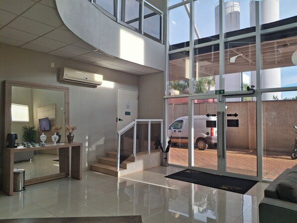 A modern hotel lobby with a reception desk, a large mirror, a staircase, and a view of the outside parking area. - Onix Inn Hotel Cravinhos (Cravinhos)