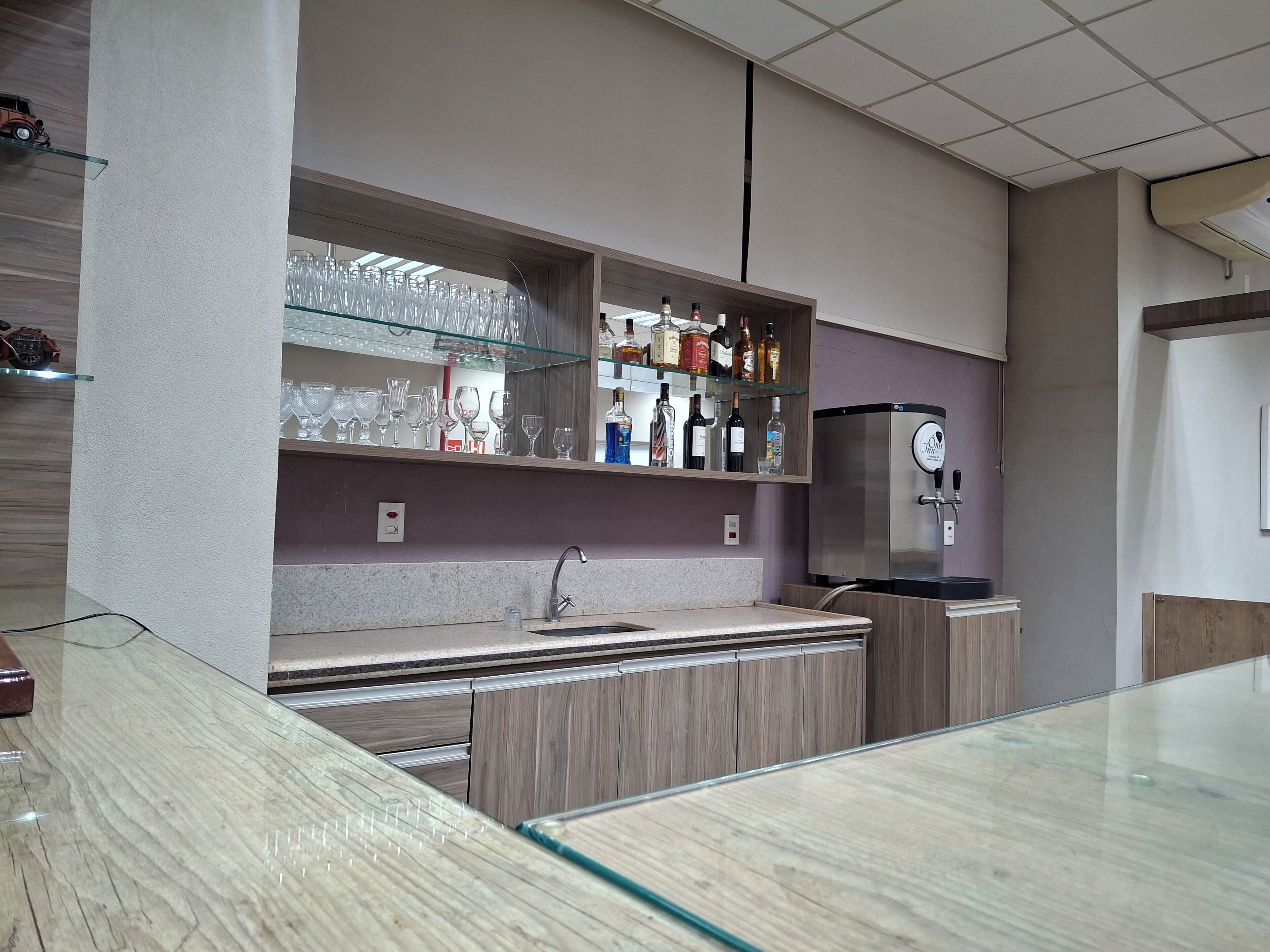 Zona de bar moderna con encimera de vidrio, pileta de acero inoxidable y un mini bar con botellas de licor.