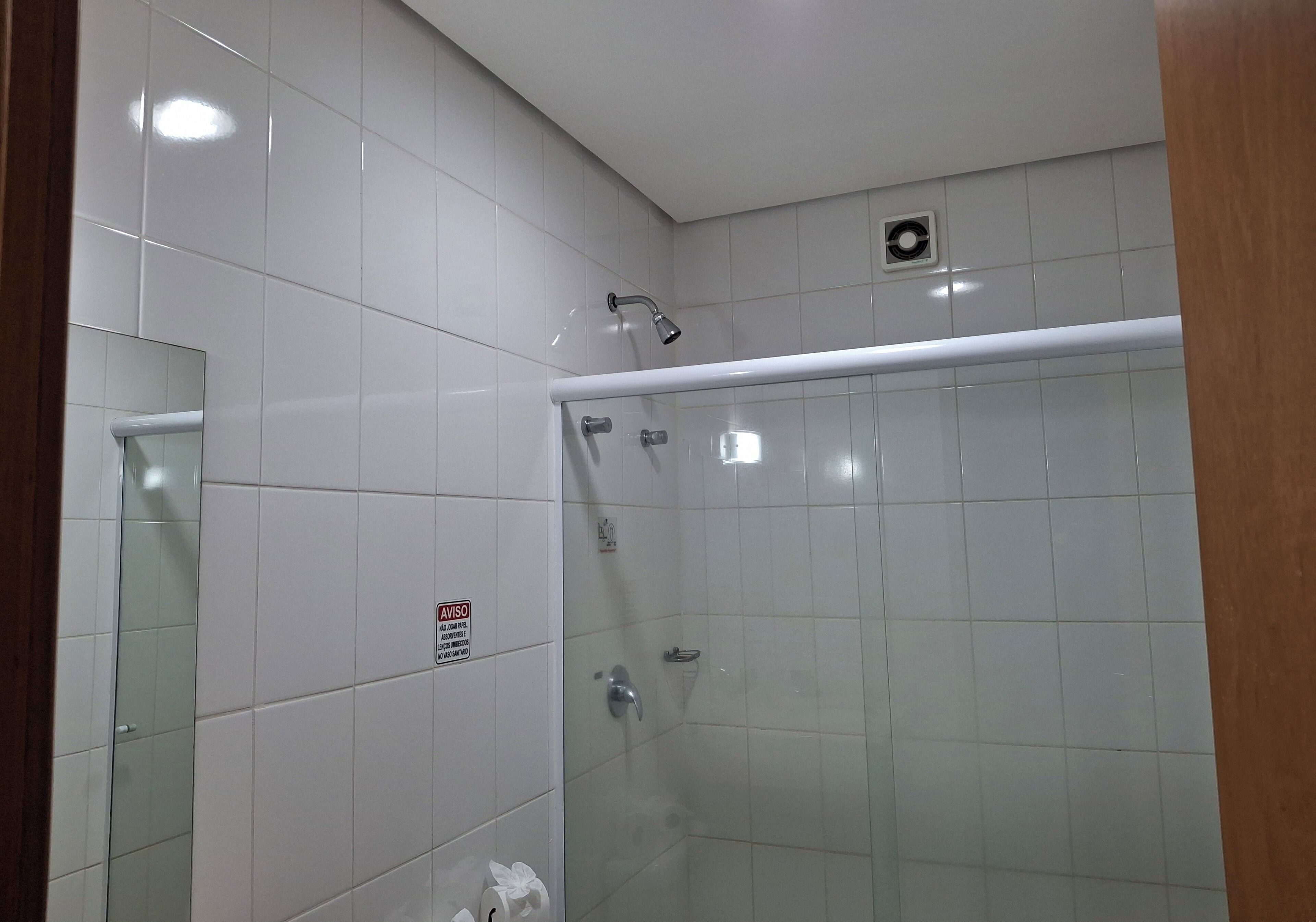 A modern bathroom with white tiles, a glass shower enclosure, a hand dryer, and a towel rack.