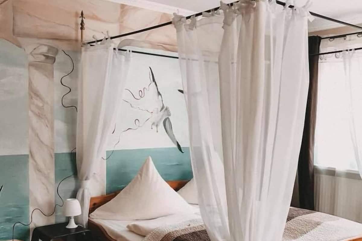 A bedroom with a wooden bed, white canopy, and a nightstand with a lamp.