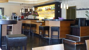 A bar area with a counter, stools, and hanging lights. - Hotel Ammerländer Hof (Westerstede)